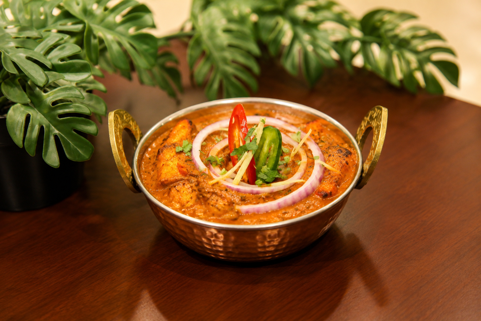 Paneer tikka masala in a copper kadai with onion rings, green and red chilli and ginger