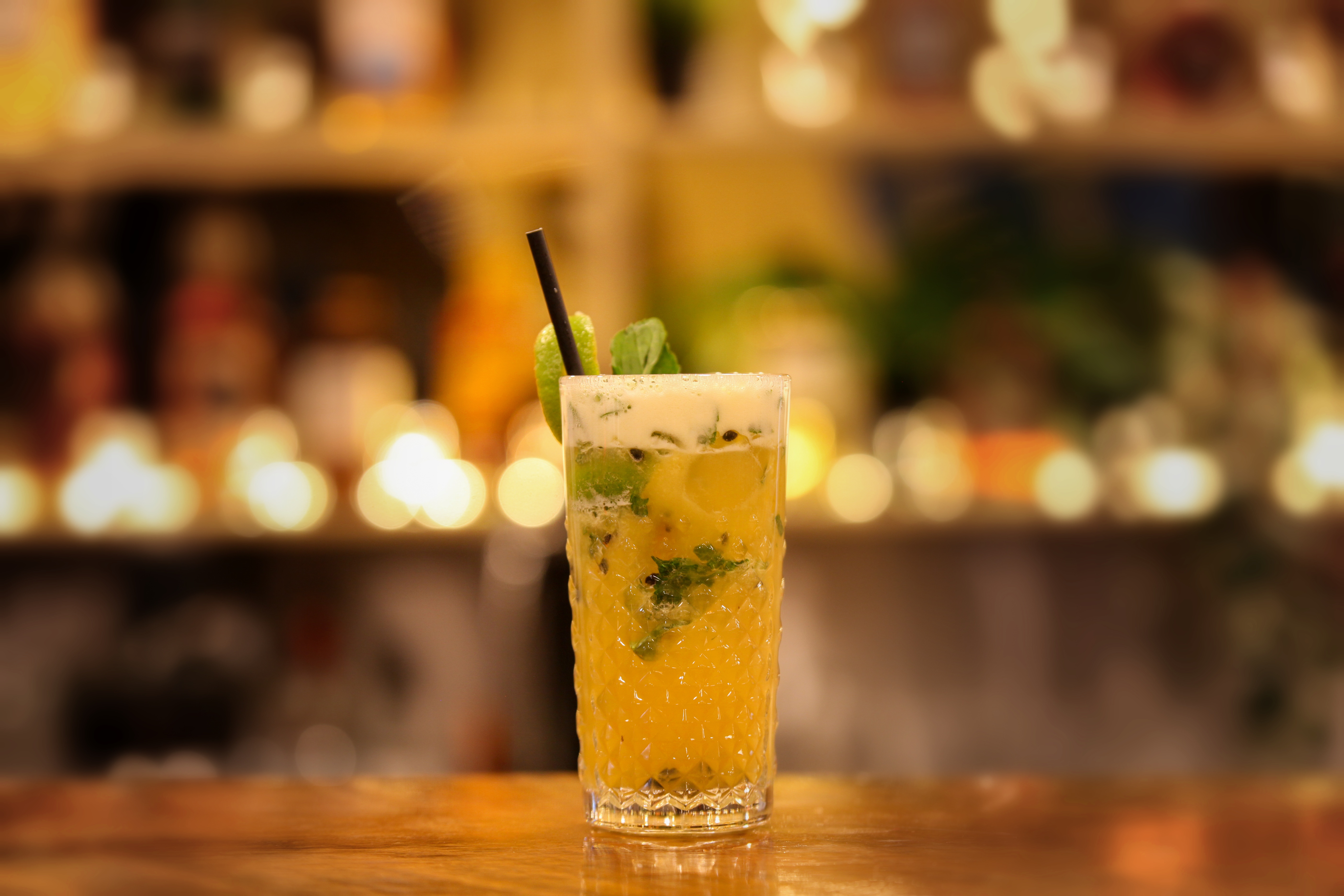 Tropical fizz in a cut-crystal glass with passionfruit, mint and a lime twist, glowing bar shelves behind