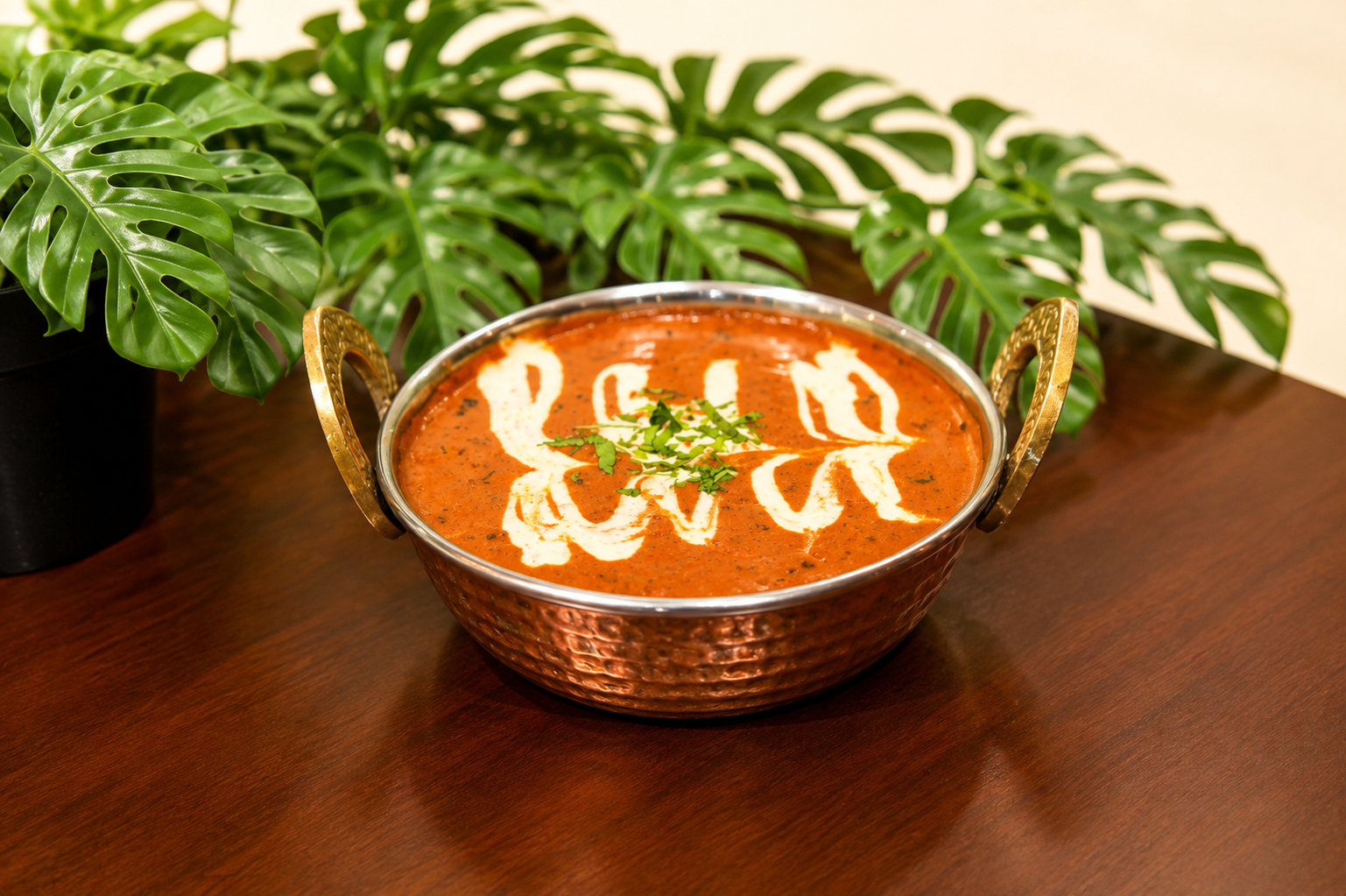 Daal makhani in a hammered copper kadai with a cream swirl and chopped coriander, monstera plant behind