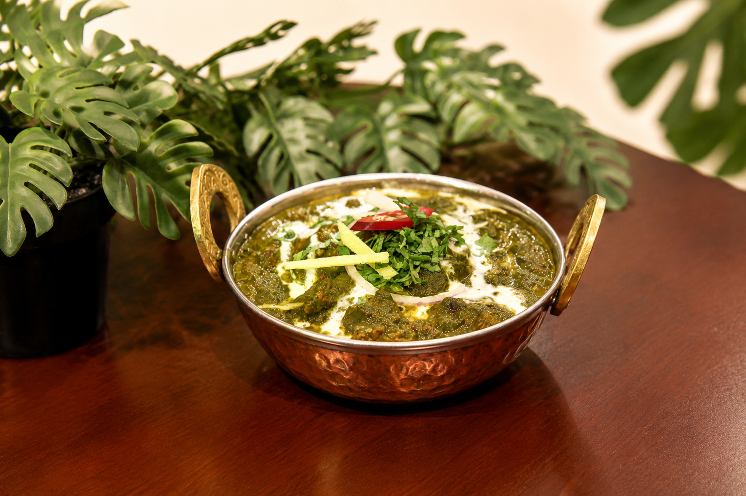 Palak chicken in a hammered copper kadai with a cream drizzle, red onion, ginger and red chilli, monstera plant behind