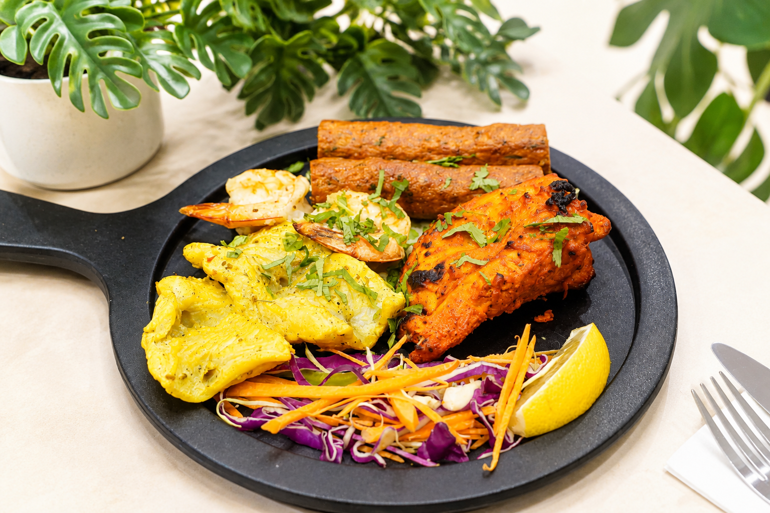 Non-veg platter with chicken tikka, prawns and seekh kebabs on a black round serving board